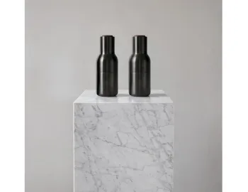 Two dark metallic Audo Bottle Grinders standing on a pale veined square plinth