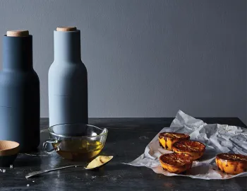 Dark and pale blue Audo Bottle Grinders beside oil, mustard and roasted citrus on a dark surface