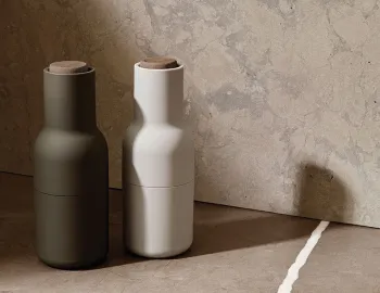 Hunting green and off-white Audo Bottle Grinders with wooden lids against a textured stone backdrop