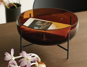 Amber Échasse Bowl holding a book on a wooden table, with its dark supporting stand visible