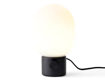 Black JWDA Table Lamp illuminated, with a glowing rounded shade above its cylindrical base