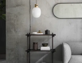 Black oval Norm Wall Mirror hung horizontally above a dark shelving unit beside a grey sofa