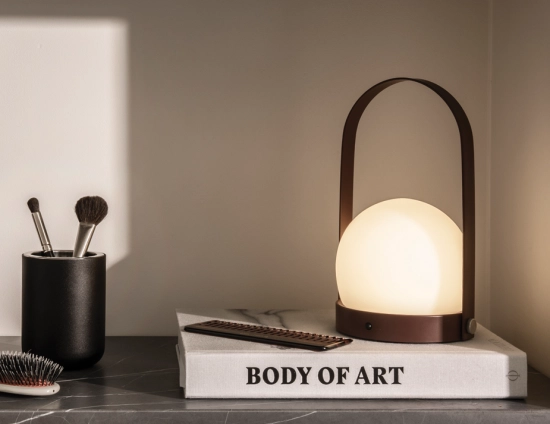 Burned red Carrie Table Lamp glowing on a book beside a comb, brushes and a black container
