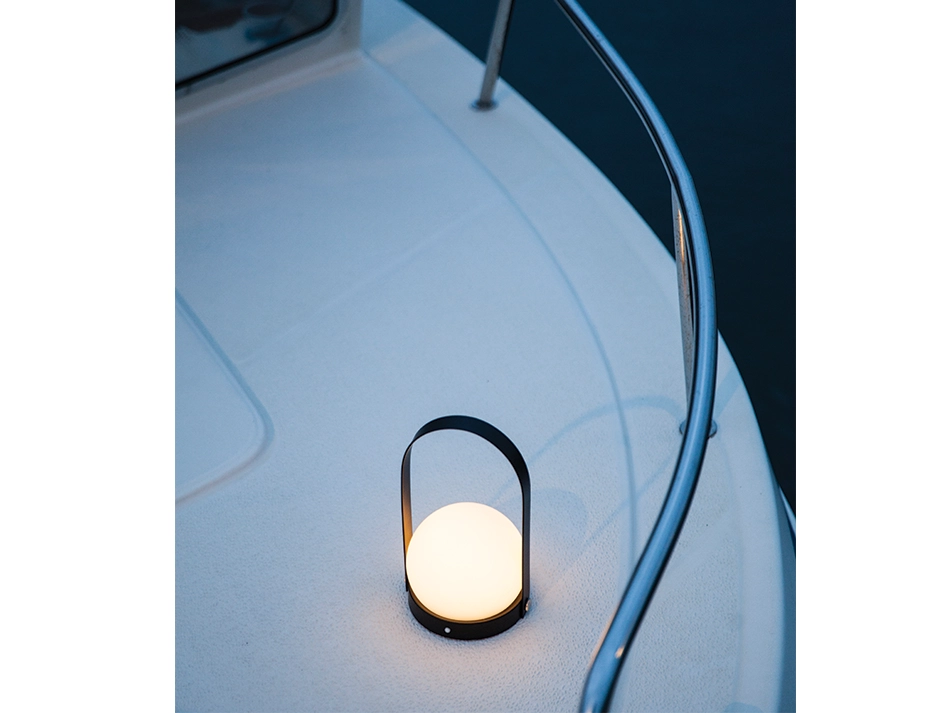 Black Carrie Table Lamp glowing on the deck of a boat beside a curved railing at dusk
